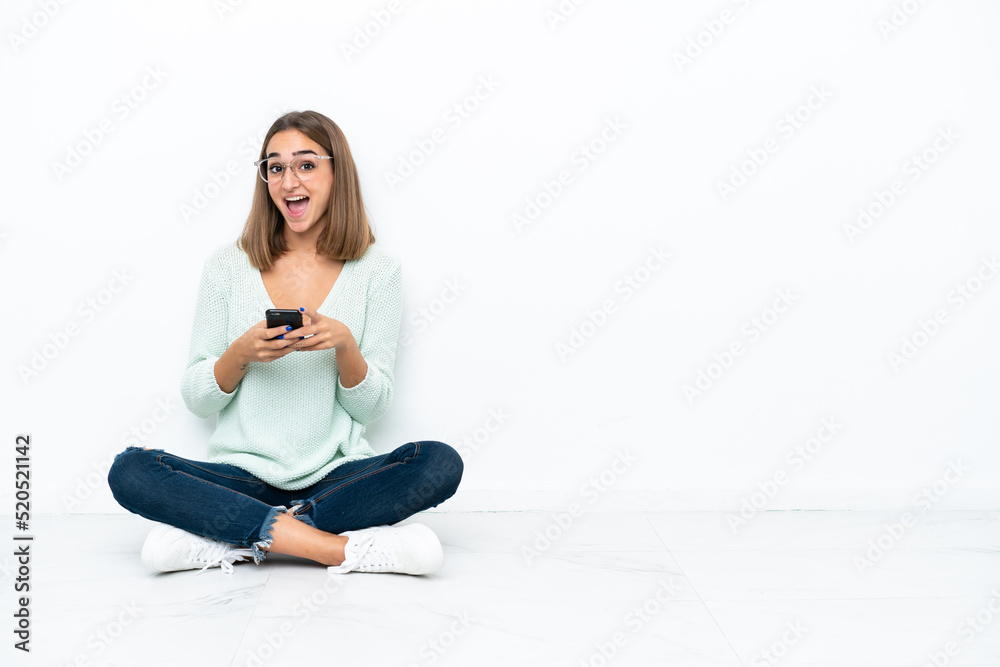 Young caucasian woman sitting on the floor isolated on white background surprised and sending a message Young caucasian woman sitting on the floor isolated on white background surprised and sending a message