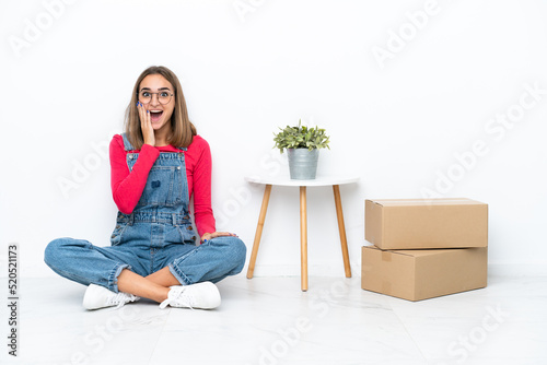 Young caucasian woman sitting on the floor among boxes with surprise and shocked facial expression