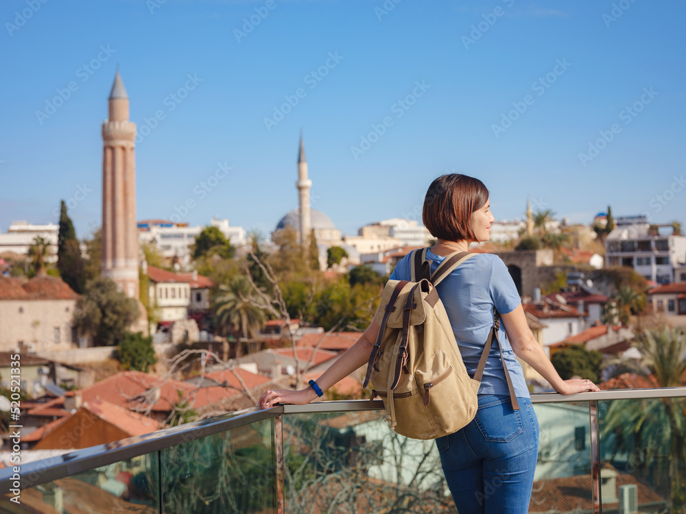 travel to Turkey, old town Antalya Kaleci. Happy asian female tourist traveller with backpack walks in old city. Woman on lookout over the old town and the port from viewpoint