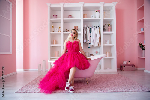 Fotografia blond happy girl  in pink dress and sneakers sitting in pink boudoir with bath i