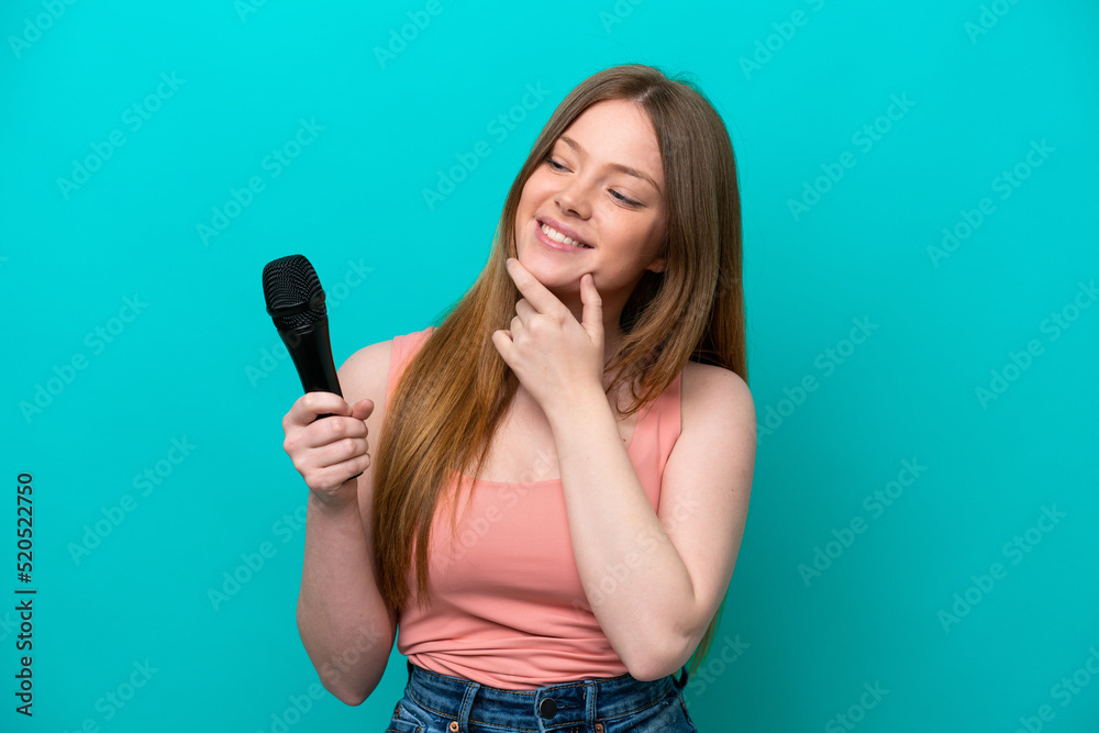 Singer caucasian woman picking up a microphone isolated on blue background looking to the side and smiling Singer caucasian woman picking up a microphone isolated on blue background looking to the side and smiling