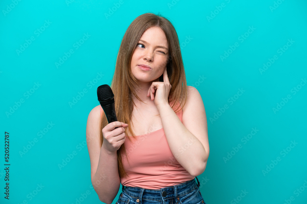 Singer caucasian woman picking up a microphone isolated on blue background frustrated and covering ears Singer caucasian woman picking up a microphone isolated on blue background frustrated and covering ears