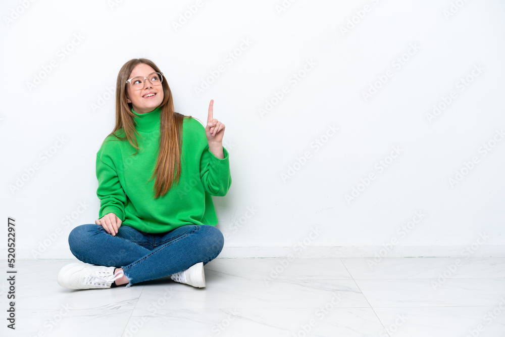 Young caucasian woman sitting on the floor isolated on white background pointing up and surprised Young caucasian woman sitting on the floor isolated on white background pointing up and surprised