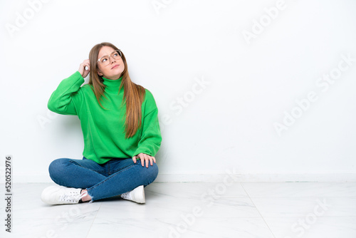 Young caucasian woman sitting on the floor isolated on white background having doubts and with confuse face expression