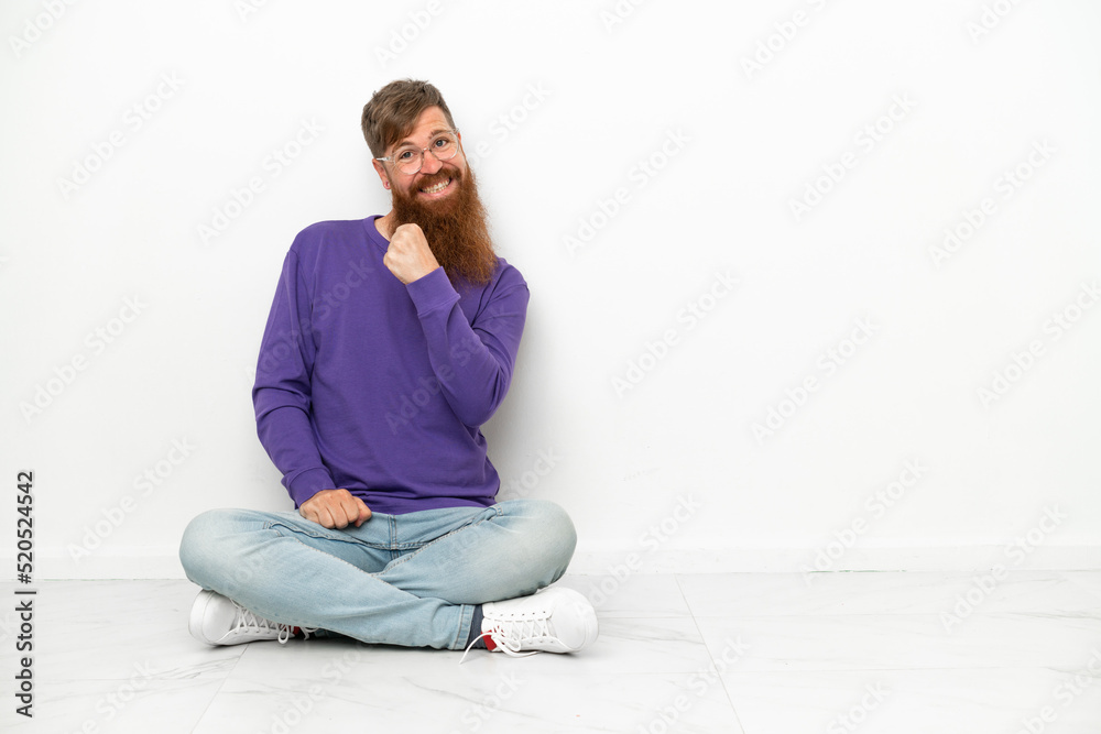 Young caucasian reddish man sitting on the floor isolated on white background celebrating a victory