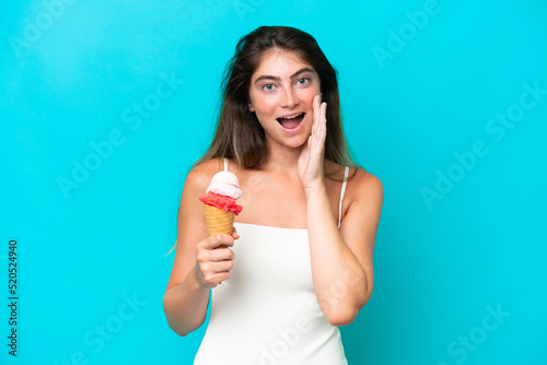 Young woman in swimsuit holding an ice cream isolated on blue background shouting with mouth wide open