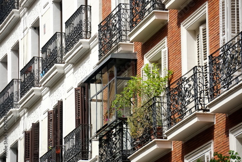 The facade of typical Spanish old house with beautiful balcony with various green plants in summer. Balcony with metal railings.