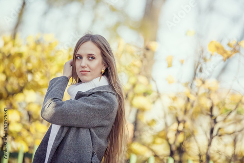 Portrait of a pretty young woman with light brown hair. Beautiful woman in an autumn park against a background of yellow foliage. Fall season.