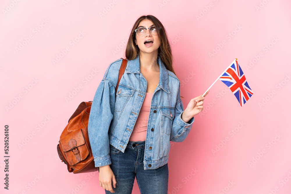 Young woman holding an United Kingdom flag isolated on pink background looking up and with surprised expression Young woman holding an United Kingdom flag isolated on pink background looking up and with surprised expression