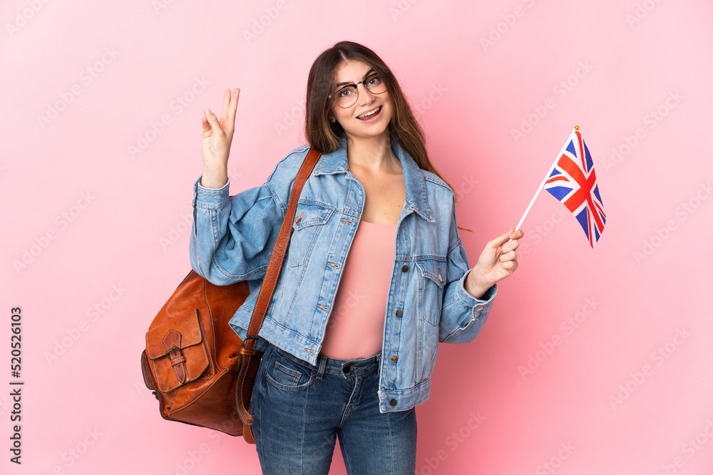 Young woman holding an United Kingdom flag isolated on pink background smiling and showing victory sign Young woman holding an United Kingdom flag isolated on pink background smiling and showing victory sign