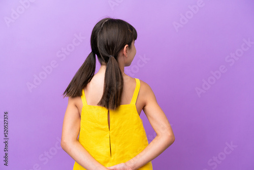 Little caucasian kid isolated on purple background in back position and looking back