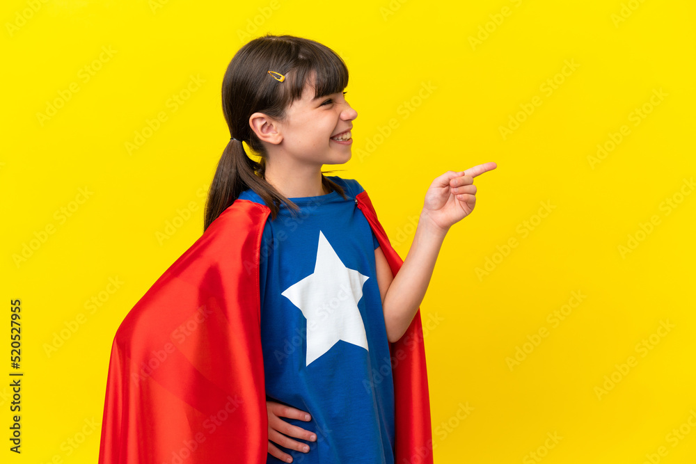 Little super hero kid isolated on purple background pointing finger to the side and presenting a product Little super hero kid isolated on purple background pointing finger to the side and presenting a product