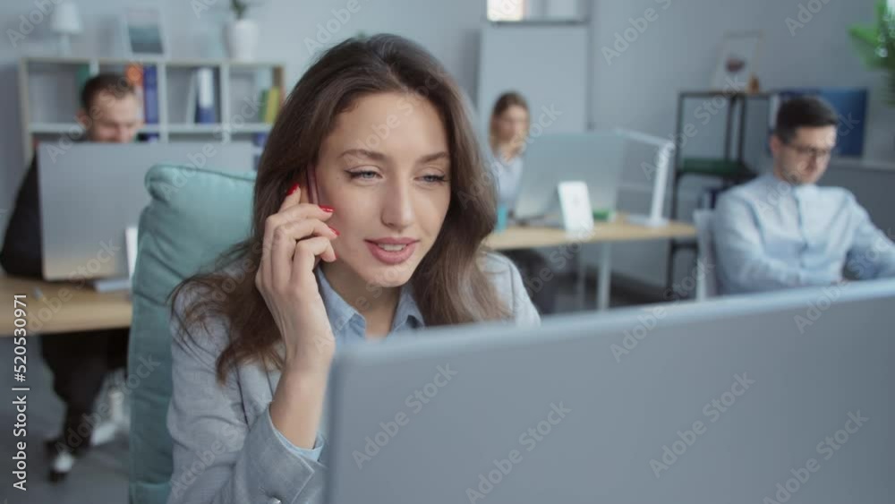 Attractive businesswoman speaks on phone working on laptop computer. On background people working. Portrait. Close up Attractive businesswoman speaks on phone working on laptop computer. On background people working. Portrait. Close up