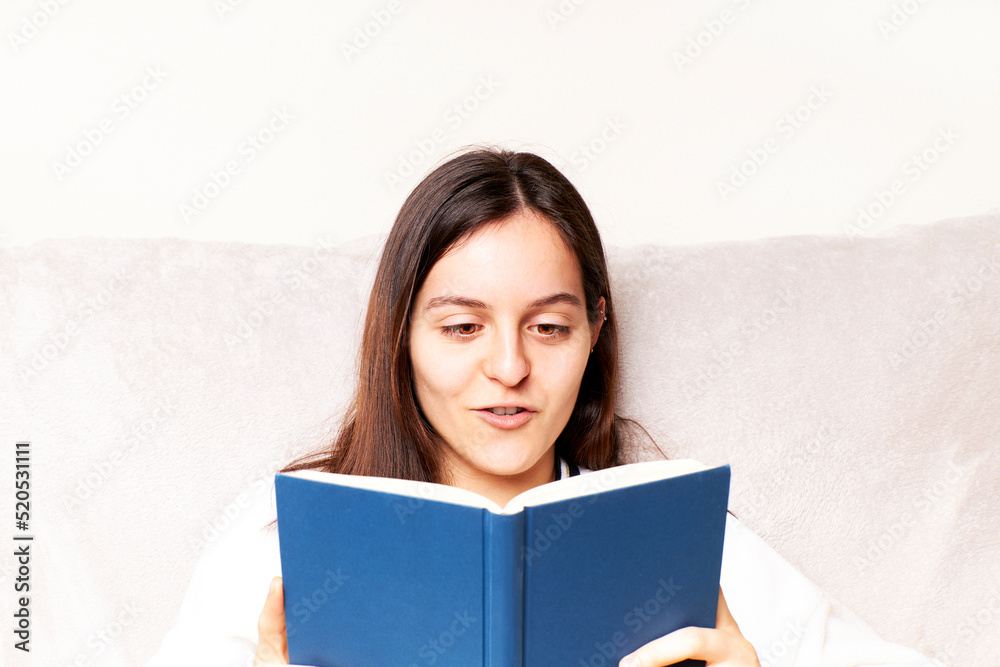 Young woman reading a book and gesturing sitting on the couch at home. Fun concept Young woman reading a book and gesturing sitting on the couch at home. Fun concept