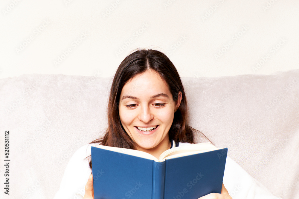 Young woman reading a book and gesturing sitting on the couch at home Young woman reading a book and gesturing sitting on the couch at home
