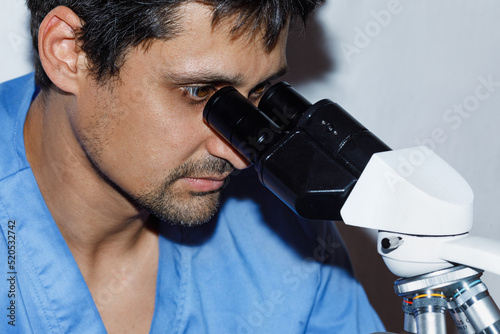 A brunette histologist doctor in a blue medical uniform looks in a professional microscope for a biopsy diagnosis. photo