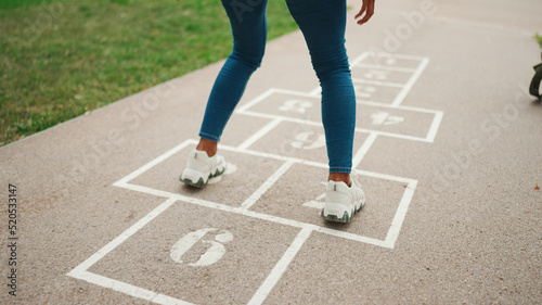 Close-up of young woman hopscotching on city playground. Closeup of the legs of girl jumping on the drawn cells on the pavement