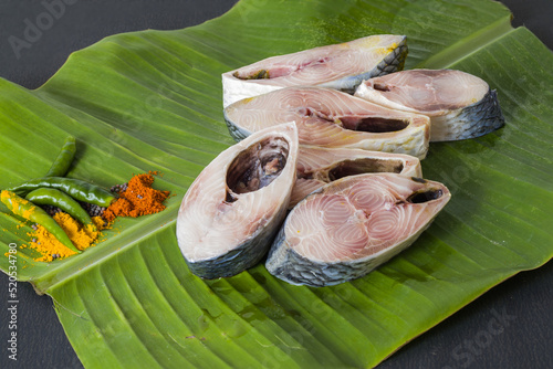 Raw hilsa fish cut into pieces kept on banana leaf for cooking. Shot taken in studio with copy space background and spices. photo