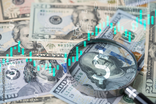 Closeup on magnifier glass with Benjamin Franklin on US dollar banknote and stock market graph for currency exchange and Interest rates concept.