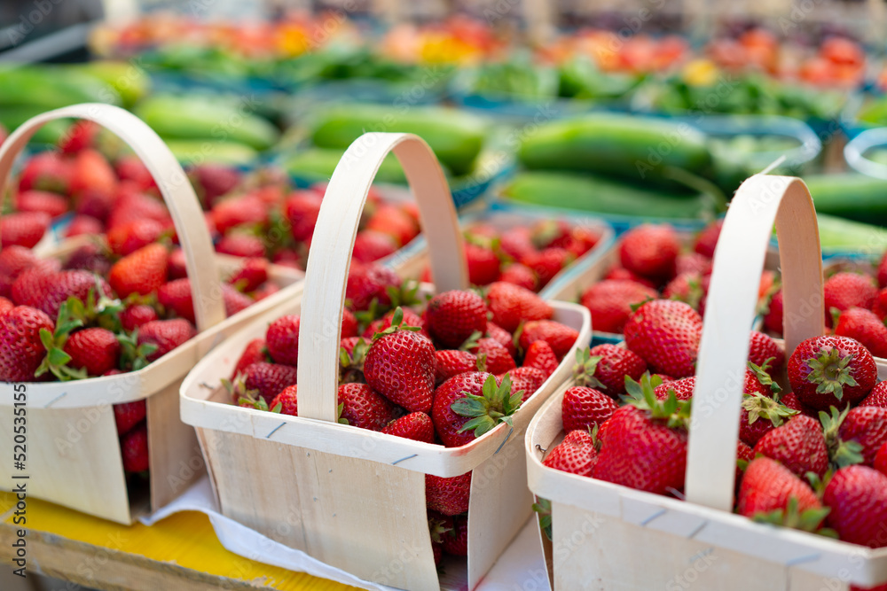 Strawberries for sale on vegetables market. Raw juicy strawberry in wooden basket standing on market display with other fruit and berry on background Strawberries for sale on vegetables market. Raw juicy strawberry in wooden basket standing on market display with other fruit and berry on background