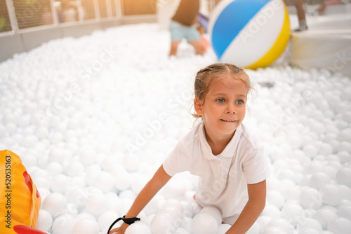 Happy little girl playing white plastic balls pool in amusement park. playground for kids. photo