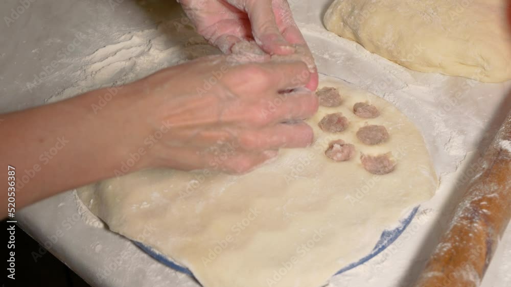A woman sculpts dumplings using a plastic mold. The girl puts minced meat into the cells of the form for making dumplings. Close-up, selective focus.