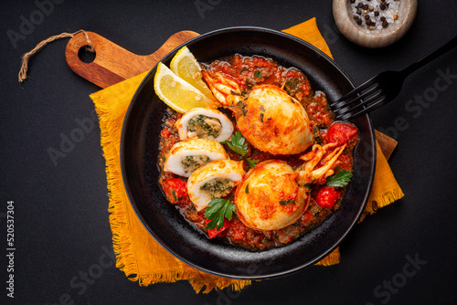 Sepia, calamari or Cuttlefish stuffed with swiss chard, bread crumbs and parmesan cheese and cooked in tomato sauce. Black background. Directly above.
