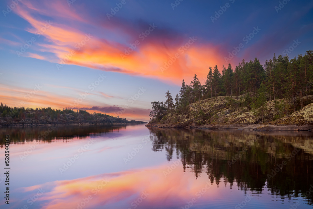 Karelian landscapes. Ladoga lake. Regions Russia. Pine trees on shore Lake Ladoga. Sunset in wild. Rocky coast Karelian lakes. Pine forest is reflected in water. Karelian Republic. Russian Federation