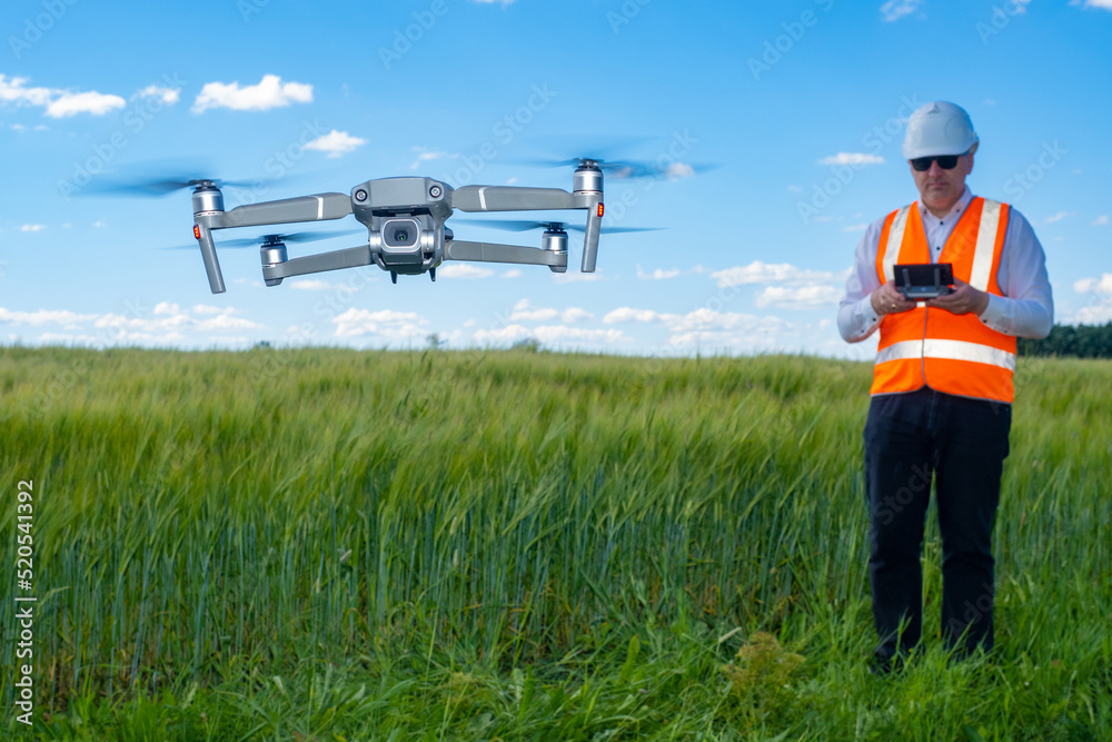 Surveyor with quadrocopter. Geodetic research before construction. Man in work uniform admits quadcopter. Modern geodetic drone. Surveyor quadcopter over field of grass. Surveyor services. Art focus Surveyor with quadrocopter. Geodetic research before construction. Man in work uniform admits quadcopter. Modern geodetic drone. Surveyor quadcopter over field of grass. Surveyor services. Art focus