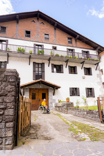 Portrait of a disabled person in a wheelchair next to a beautiful rural house