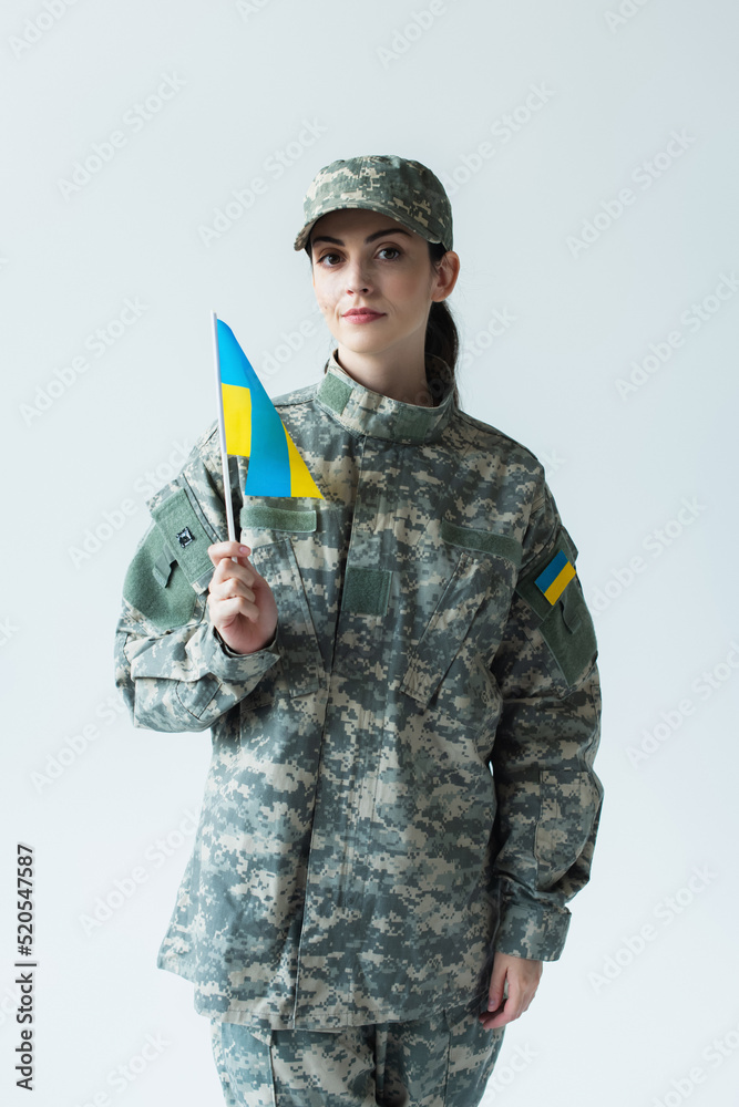 Young soldier holding ukrainian flag and looking at camera isolated on grey Young soldier holding ukrainian flag and looking at camera isolated on grey