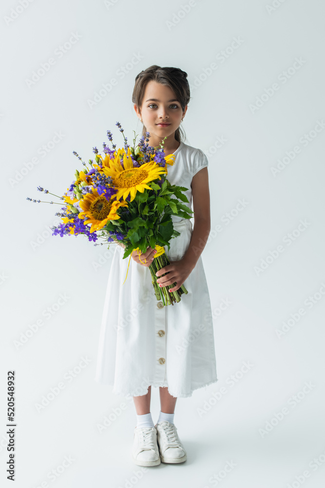 Full length of child holding blue and yellow bouquet on grey background Full length of child holding blue and yellow bouquet on grey background
