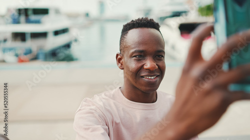 Foto Young African guy uses the phone standing on the embankment with yachts and ship