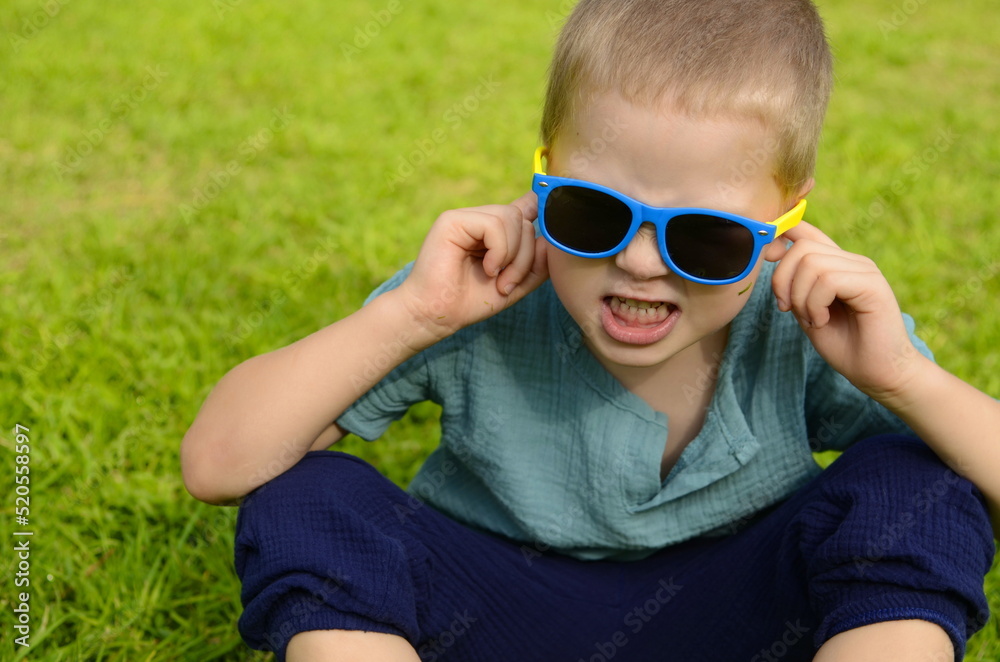 Portrait of a boy on the background of a grassy meadow. A boy in black glasses covers his ears with his hands. Concept: noise, unpleasant sound, bad music. children do not listen to parents, the stude Portrait of a boy on the background of a grassy meadow. A boy in black glasses covers his ears with his hands. Concept: noise, unpleasant sound, bad music. children do not listen to parents, the stude