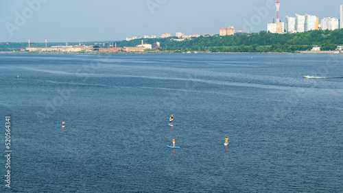 Active recreation on the board on the big river. Tourism on sap boards. Outdoor water sports. Surfers, standing on a board, ride the waves. SUP surfing training. View of the city embankment