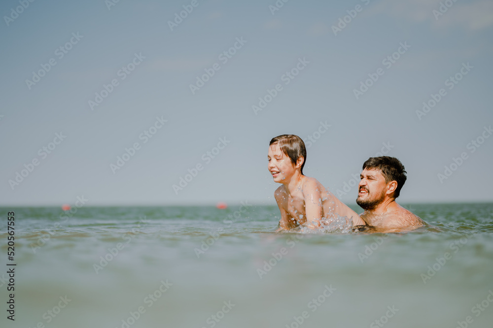 Dad swims with his son in the sea. The father throws his son in the water. The boy does a somersault in the sea. The family spends their summer vacation at the sea. Dad swims with his son in the sea. The father throws his son in the water. The boy does a somersault in the sea. The family spends their summer vacation at the sea.