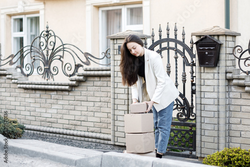 Young woman carrying parcels home, standing with a heap of cardboard boxes. Concept of buying goods online and delivering them home