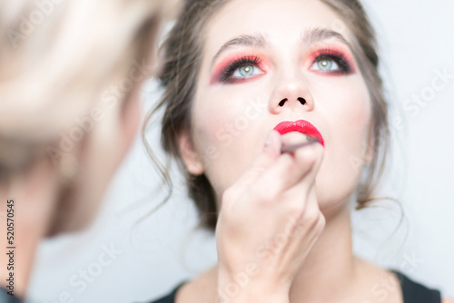 Makeup. Makeup artist applies red lipstick. Sensual lips. Close-up.