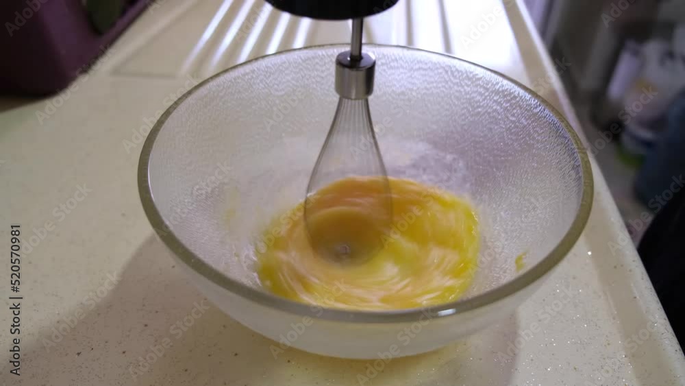 Whisking or scrambling egg with electrical mixer in a mixing bowl on the kitchen counter Whisking or scrambling egg with electrical mixer in a mixing bowl on the kitchen counter