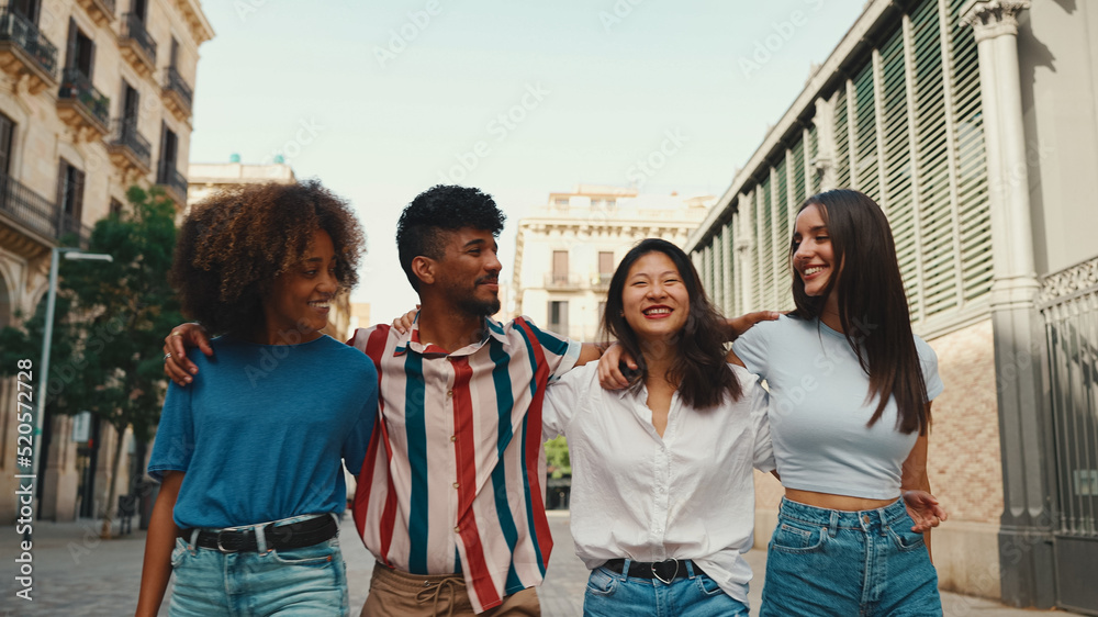 Happy multiethnic young people walk embracing on summer day outdoors. Group of friends are talking and laughing merrily while walking along on the street Happy multiethnic young people walk embracing on summer day outdoors. Group of friends are talking and laughing merrily while walking along on the street