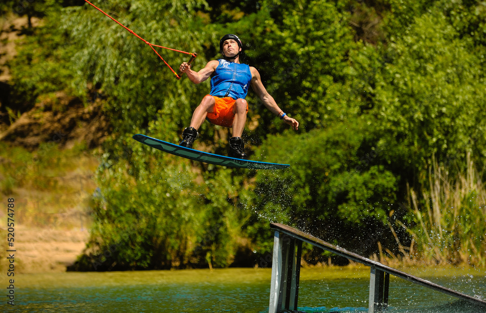 Professional wakeboarder jumping over the water against the sky and trees