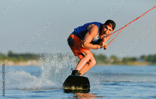 A professional wakeboarder rides on the lake in sunny weather, performing figures