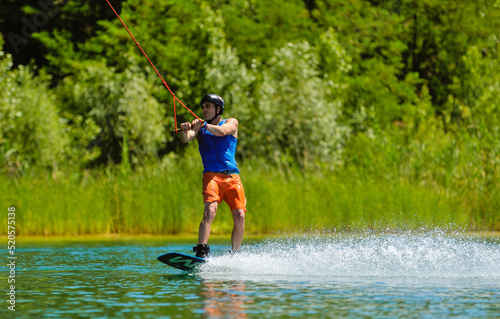 Fototapeta Naklejka Na Ścianę i Meble -  A professional wakeboarder rides on the lake in sunny weather, performing figures
