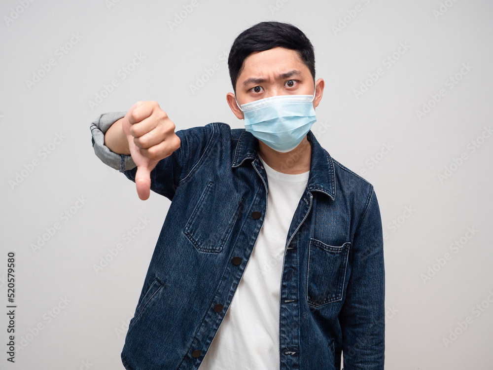 Man jeans shirt wear medical mask serious face show thumb down Man jeans shirt wear medical mask serious face show thumb down