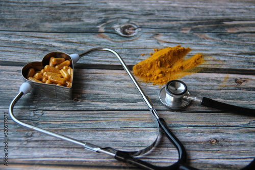 Turmeric powder and turmeric pills in a heart-shaped bowl, with a stethoscope on a wooden table, top view photo