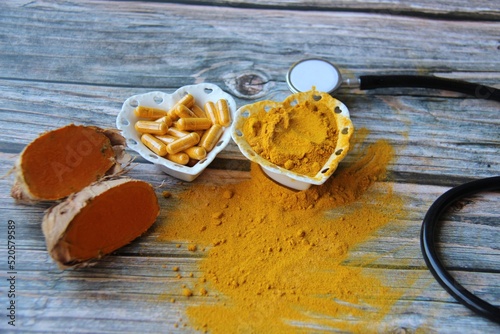 Turmeric powder, fresh organic turmeric and turmeric pills in a heart-shaped bowl with a stethoscope on a wooden table, top view. photo