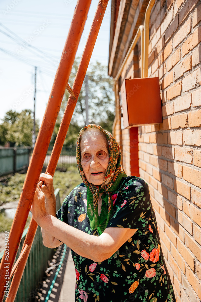 old grandmother posing for a photo near her old brick house