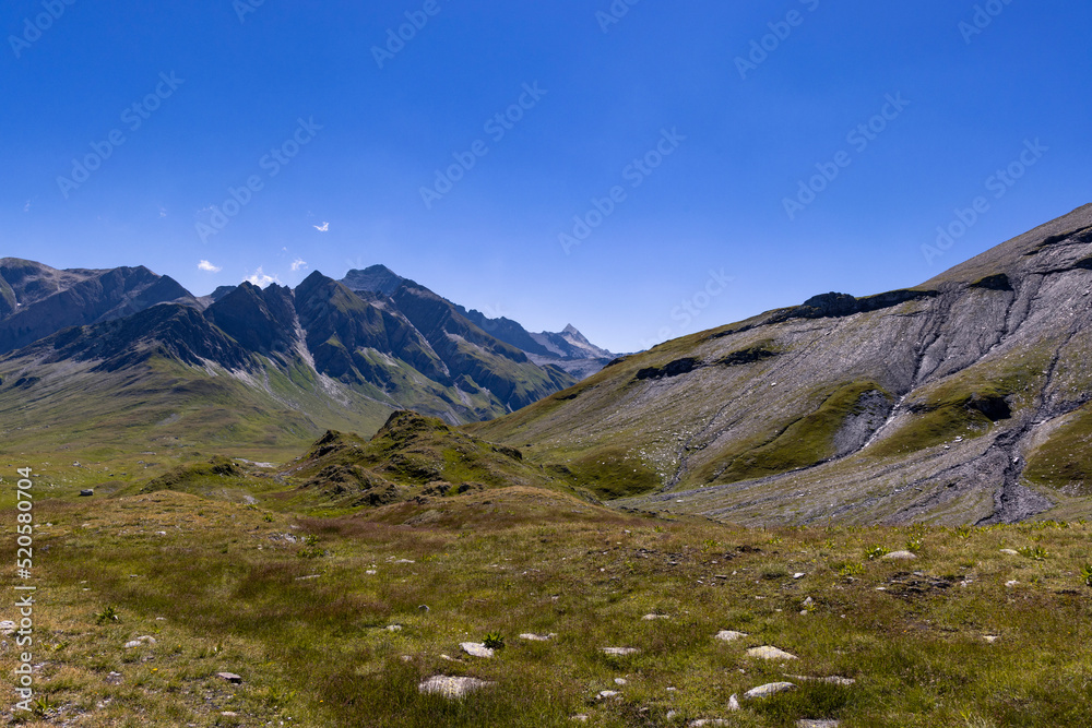 Aerial view towards the high mountains of the Greina plateau in Blenio, Swiss Alps. A rocky ridge on the right leads the eye towards the hilly valley. 