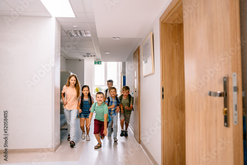 Full leight of school kids, boys and girls running to camera in elementary school hallway. photo