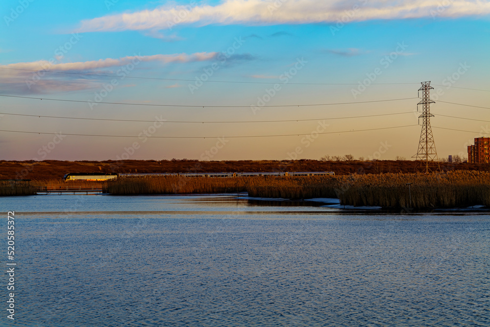 Railroad Tracks Against Sky During Sunset with blue sky, electric pylons line runs parallel to the railroad, view from water pond. High-quality photo